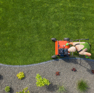 A person using a red lawnmower to cut green grass next to a landscaped gravel bed.